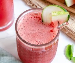watermelon cooler in tall glass cup with sliced watermelon and more cups of watermelon cooler in a white background