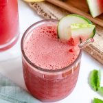 watermelon cooler in tall glass cup with sliced watermelon and more cups of watermelon cooler in a white background