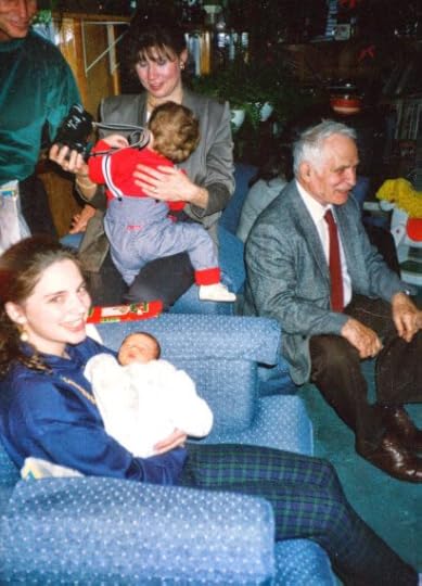 Teenage girl in blue shirt and plaid pants holding a newborn. People in the background.