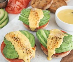 Three english muffins topped with tomato and avocado slices drizzled with vegan hollandaise sauce