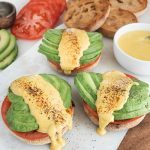 Three english muffins topped with tomato and avocado slices drizzled with vegan hollandaise sauce