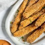 several baked zucchini fries on white platter with sauce on the side