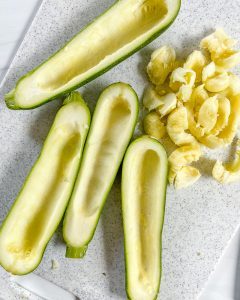 process of making zucchini boats with filling on the side of 2 sliced zucchinis on light background