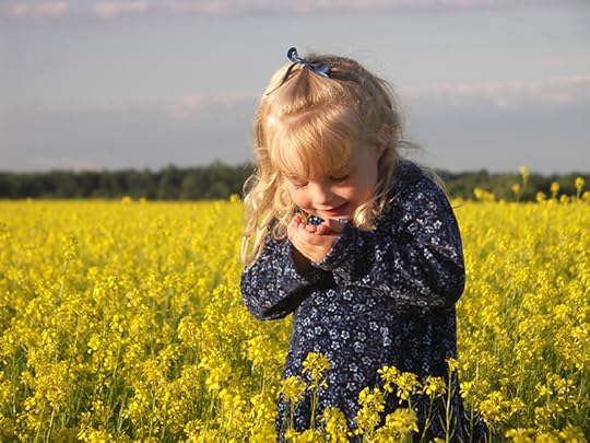 A young girl with blond hair stands in a field of yellow flowers wearing a dark blue dress and looks joyfully at something she holds in her hand. Nature's restorative properties are expressed in this phrase: