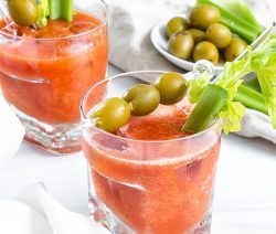2 Virgin Bloody Mary drinks in glass with decorative olives and veggies in the cup and on the side with a white background