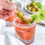 1 Virgin Bloody Mary drinks in glass with decorative olives and veggies in the cup and on the side with a white background