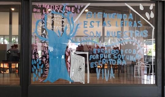 Ventanal con escritura, un árbol con hojas que se dispersan y una puerta a una casa habitada por la escritura.