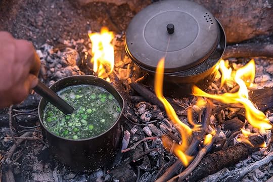Two titanium pots sit in a fire cooking food for dinner. A hand stirs the pea soup with a long spoon., backpacking food