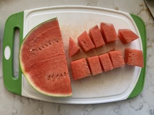 cut watermelon on a cutting board with a white marble background