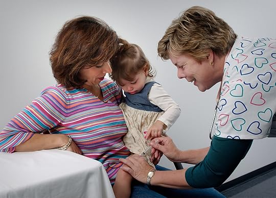 This photograph showed a young child being cradled by her mother, while she was receiving an intramuscular vaccination in her left thigh muscle. Notice that the nurse had immobilized the young girl's leg using her left hand.