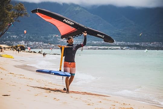 Pro wind foiler walking with kite and board on the beach