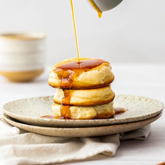 Three fluffy Japanese pancakes (aka. souffle pancakes) stacked high with maple syrup being poured on them.
