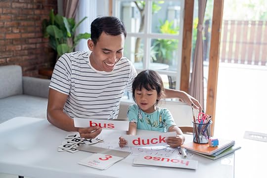 A father works with his daughter on sounding out words printed on cards. By studying the genetics of dyslexia, researchers can help more children receive an early diagnosis so they can get the academic help they need.