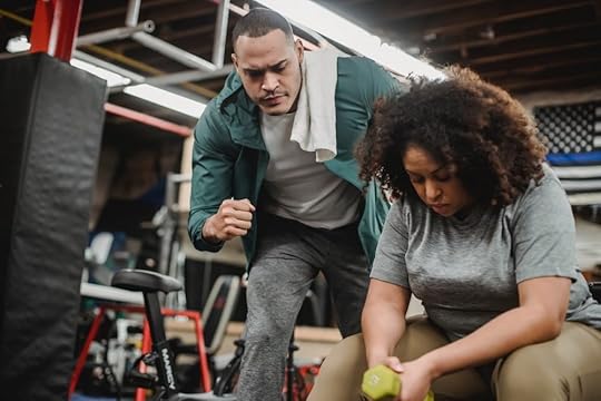 Image: a woman lifts weights at a gym while her coach stands nearby, encouraging her.