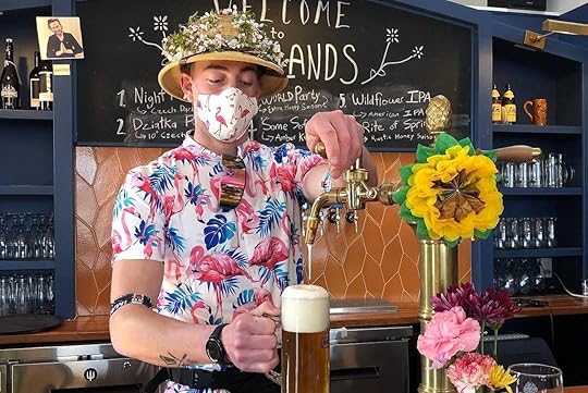 Bartender in bright shirt and flower-bedecked hat pours a pint at Otherlands Beer