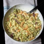pesto pasta salad in large white bowl on blue striped cloth.