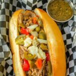 Italian beef sandwich in black checked basket with jus cup.