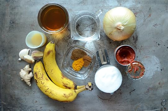 Ingredients for banana ketchup on a metal sheet pan - ginger, garlic, lemon juice, apple cider vinegar, water, onion, tomato paste, sugar, spices, and bananas.