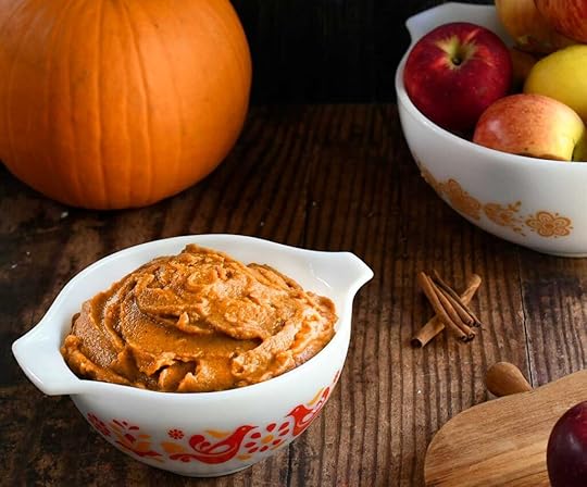 Pumpkin pie dip in a vintage white pyrex dish with red birds on it on a wooden table with a bowl of apples.