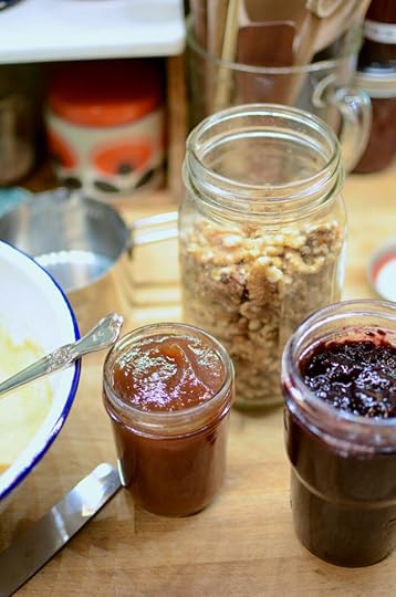 Jars of jam and walnuts on a wooden kitchen countertop.