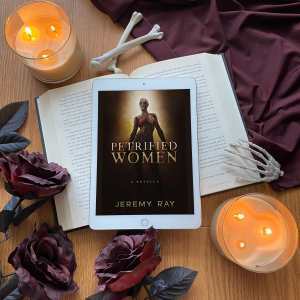 Photo of Petrified Women book surrounded by dark roses, bones, and two eerily glowing candles.