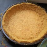 graham cracker crust in brown pie plate on work table.