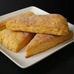 pumpkin scones stacked on white square plate on black table top.