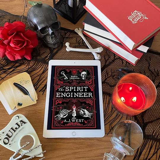 The Spirit Engineer book on iPad surrounded by red and black books, a black skull, a red rose, a ouija planchette, a red candle, and a crystal ball