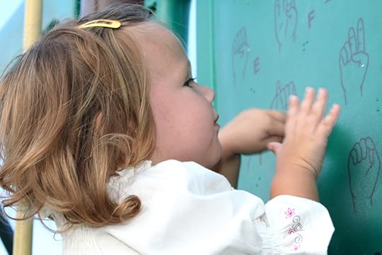 A toddler examines a chart showing the sign language alphabet and seems to be trying to make shapes with her hands. Dyslexia and the visual brain.