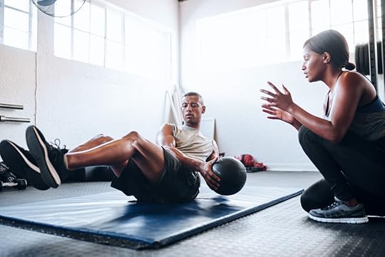 A female personal coach motivates a male client during a set of Russian twists.