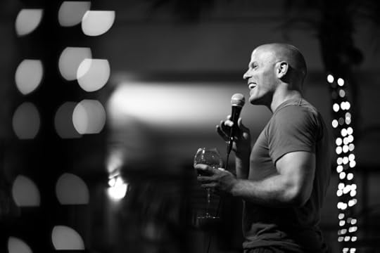 Tim Ferriss speaking at an event, smiling and holding a glass of wine.