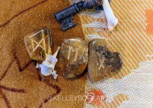 Runes Nauthiz, Ehwaz, and Dagaz with a mink vertebra on a deer skin background by S. Kelley Harrell