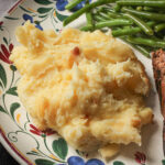 close up of a scoop of mashed potato casserole on a flowered dinner plate.