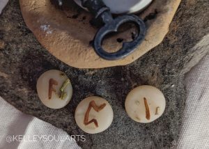 The runes Isa, Perthro, then Ansuz rest on a flat stone with an old iron key above them
