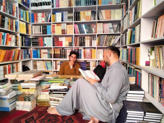 Two men sit in a small room, lined with books from floor to ceiling.