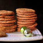 stacks of molasses crinkle cookies on square white tray with mini christmas balls nearby.