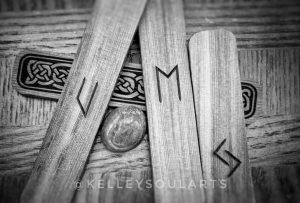 Black and white photo of cedar runes Jera, Ehwaz, then Uruz reversed, with sodalite on a wooden background