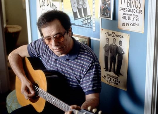 Actor Edward James Olmos sits and plays the guitar, seating, wearing a striped blue knit shirt