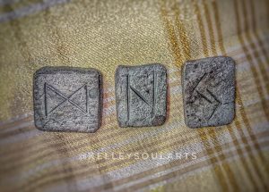 Wrought iron runes Jera, Hagalaz, and Dagaz lie on a white and plaid metallic gold background