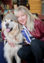 An image of Louisa with her golden retriever. The dog is wearing a deerstalker hat.