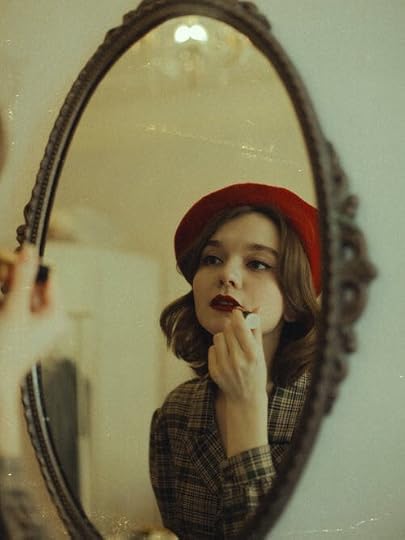 A woman, who is wearing a red beret, is applying red lipstick using a mirror.