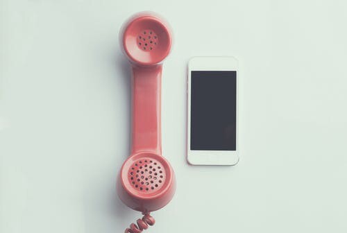A red phone receiver on the left and a white smartphone on the right.