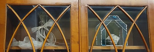 A tarnished silver vase wrapped with ribbon and a stained glass ornament sit in a wooden cabinet. What is home to you?