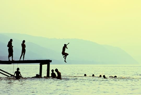 Silhouettes of kids who jump off dock on the lake at sunset.