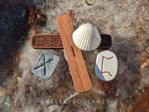 Clay rune Perthro, with cedar runes Isa and Gebo and a white seashell lying on a background of ice with leaves frozen beneath it