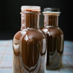 two bottles of chocolate syrup on a plaid mat.