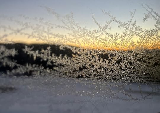 View of a snowy field and mountains through a frost-covered window.