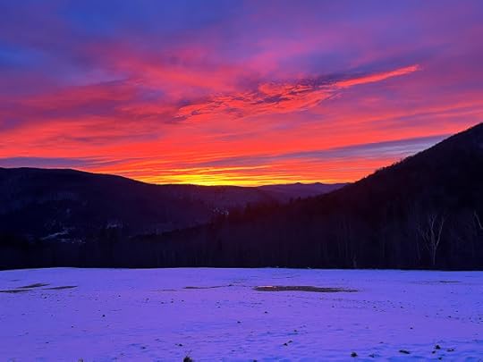 A vibrant purple, pink, and gold sunrise over a range of mountains, with a field of snow in the foreground.