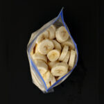 open freezer bag of frozen banana slices on black table top.