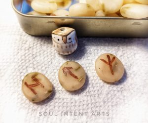 The Elder Futhark runes Algiz, Tiwaz, and Hagalaz in polymer clay, with a small ceramic owl beside a tin full of runes.